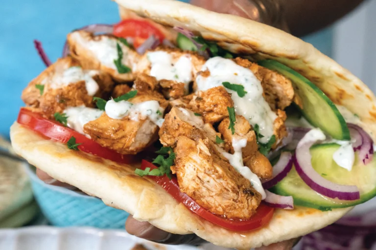 Zelfgemaakt flatbread belegd met gekruide kip, yoghurtsaus, tomaat, komkommer en rode ui.